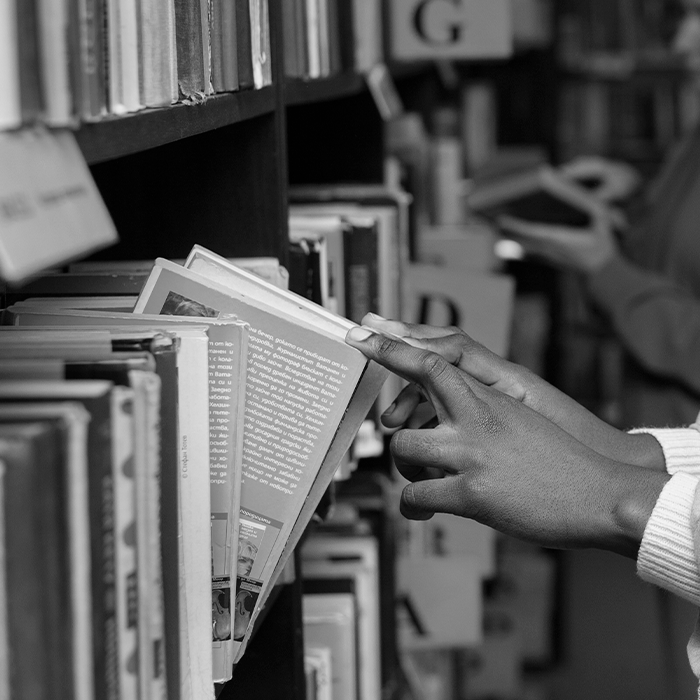 Foto em preto e branco mostra pessoa pegando livro em biblioteca