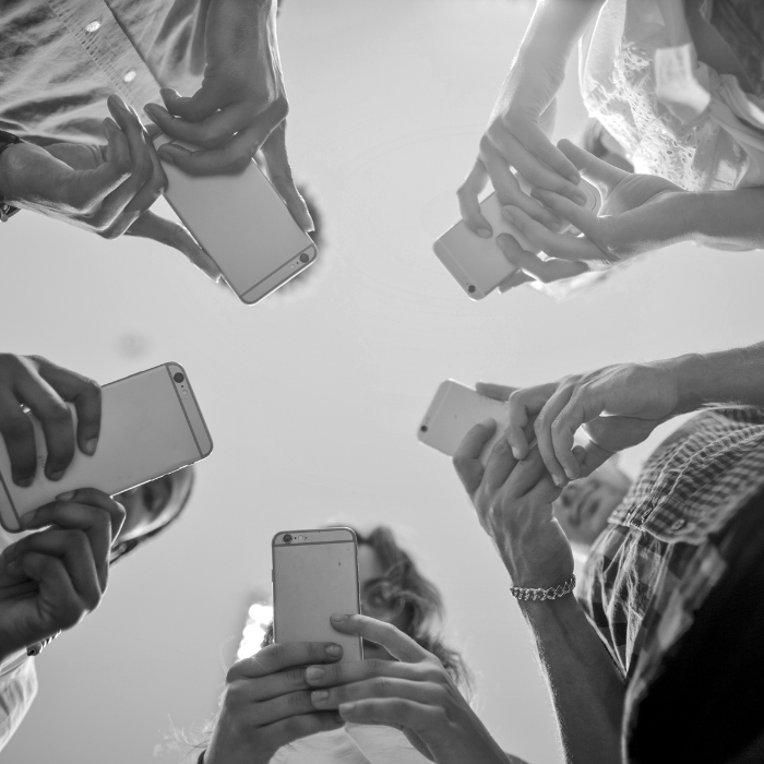 Foto em preto e branco mostra grupo de jovens compartilhando informações pelo celular